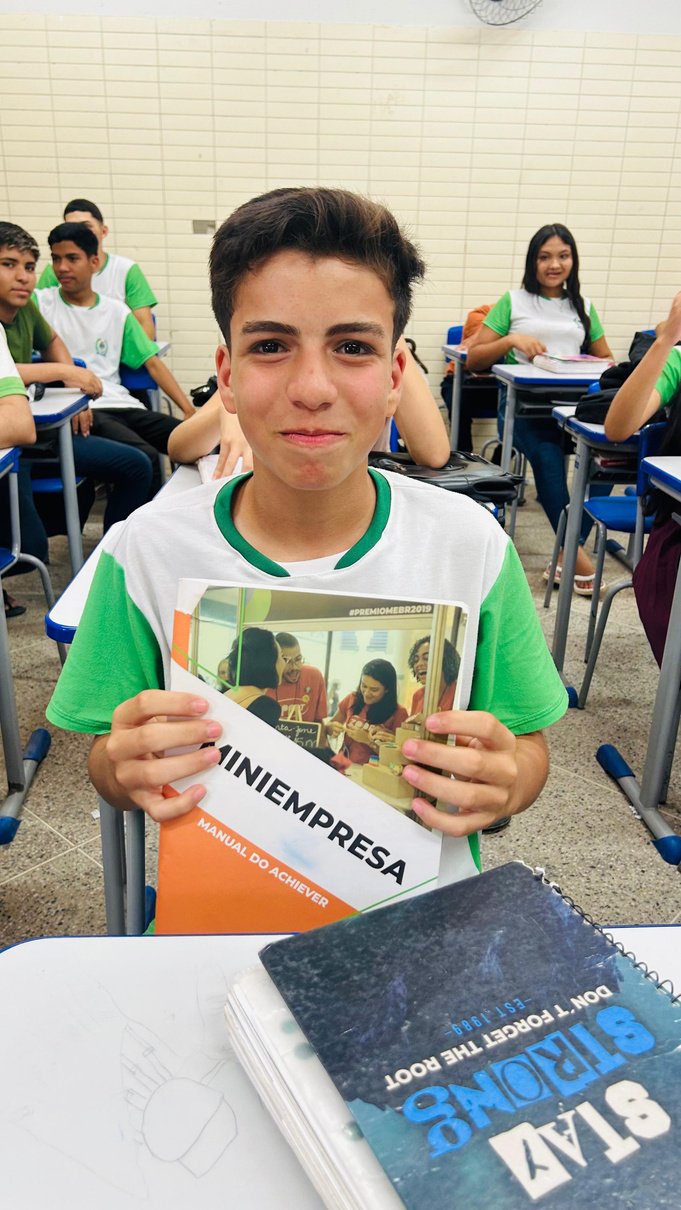 Estudante em sala de aula apresenta o manual do programa Miniempresa.