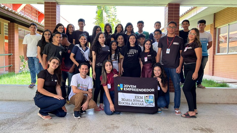 Turma de estudantes e educadores reunida com a identificação do projeto Jovem Empreendedor.